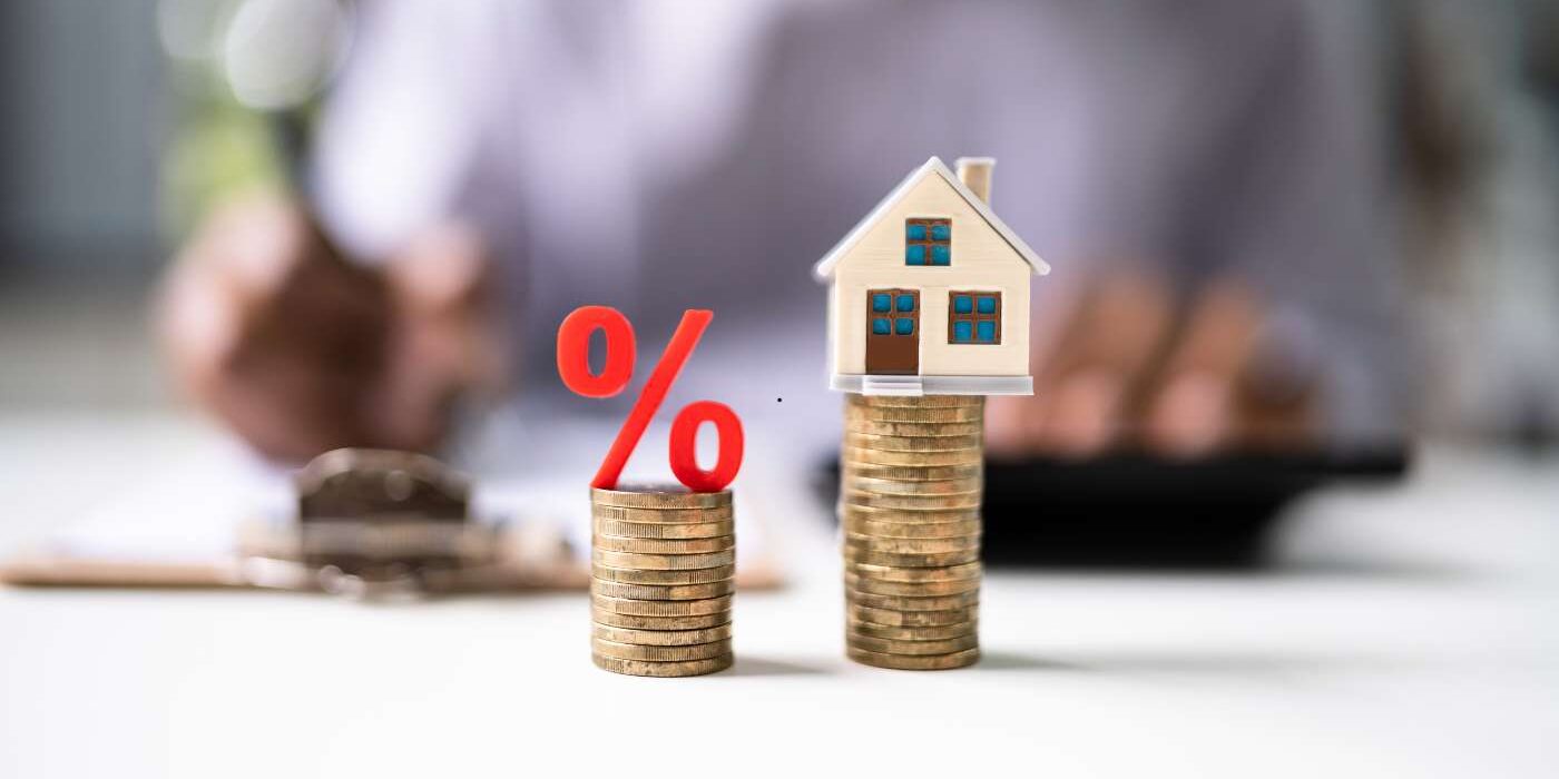 a red percentage symbol and a miniature house on top, representing interest rates and real estate investment or mortgage approvals.